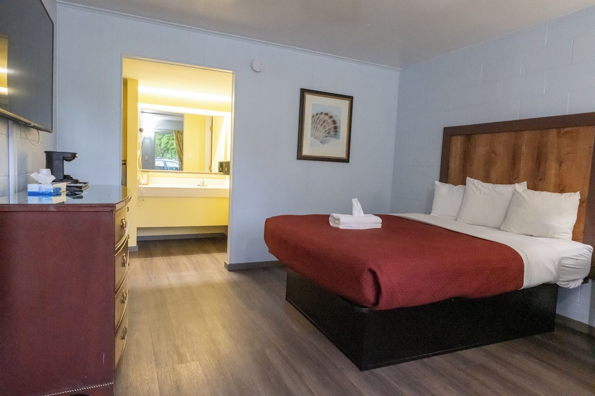 Ein Hotelzimmer mit Bett, Schreibtisch und einem durchgegangenen Tür sichtbaren Badezimmer.