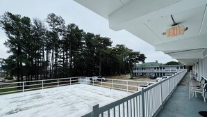 Un espace extérieur abrité, doté d’une rambarde blanche, d’un panneau indiquant la sortie et offrant une vue sur un immeuble avec un balcon.