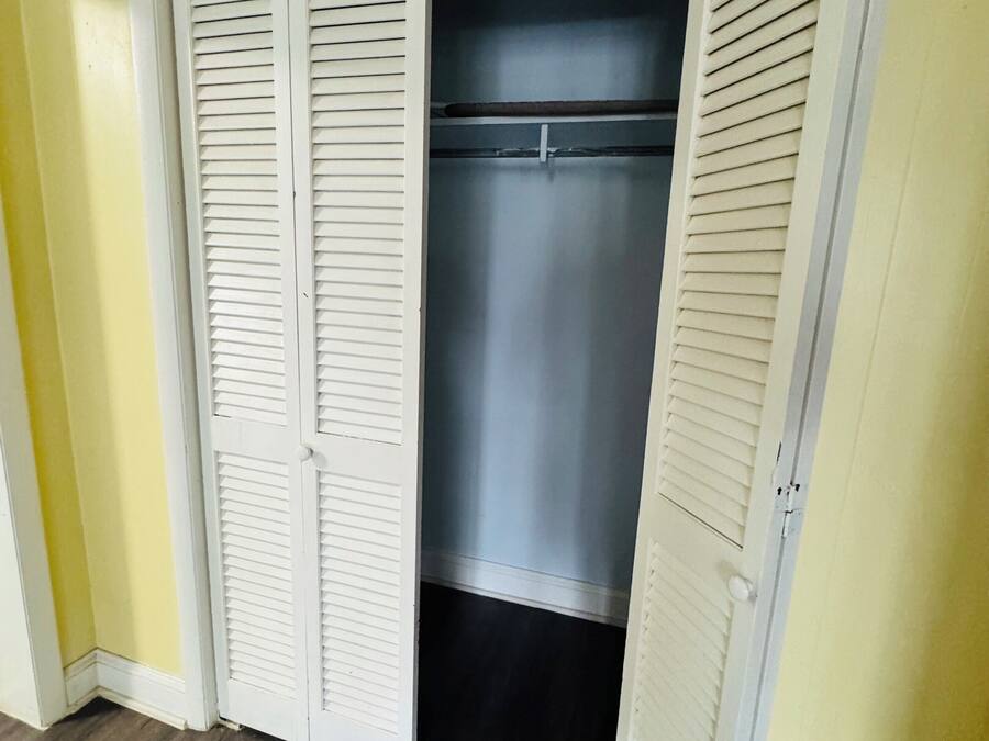 A walk-in closet with white louvered doors and a dark interior.