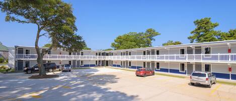A motel with a two-story structure, a parking lot, and a tree in the foreground.