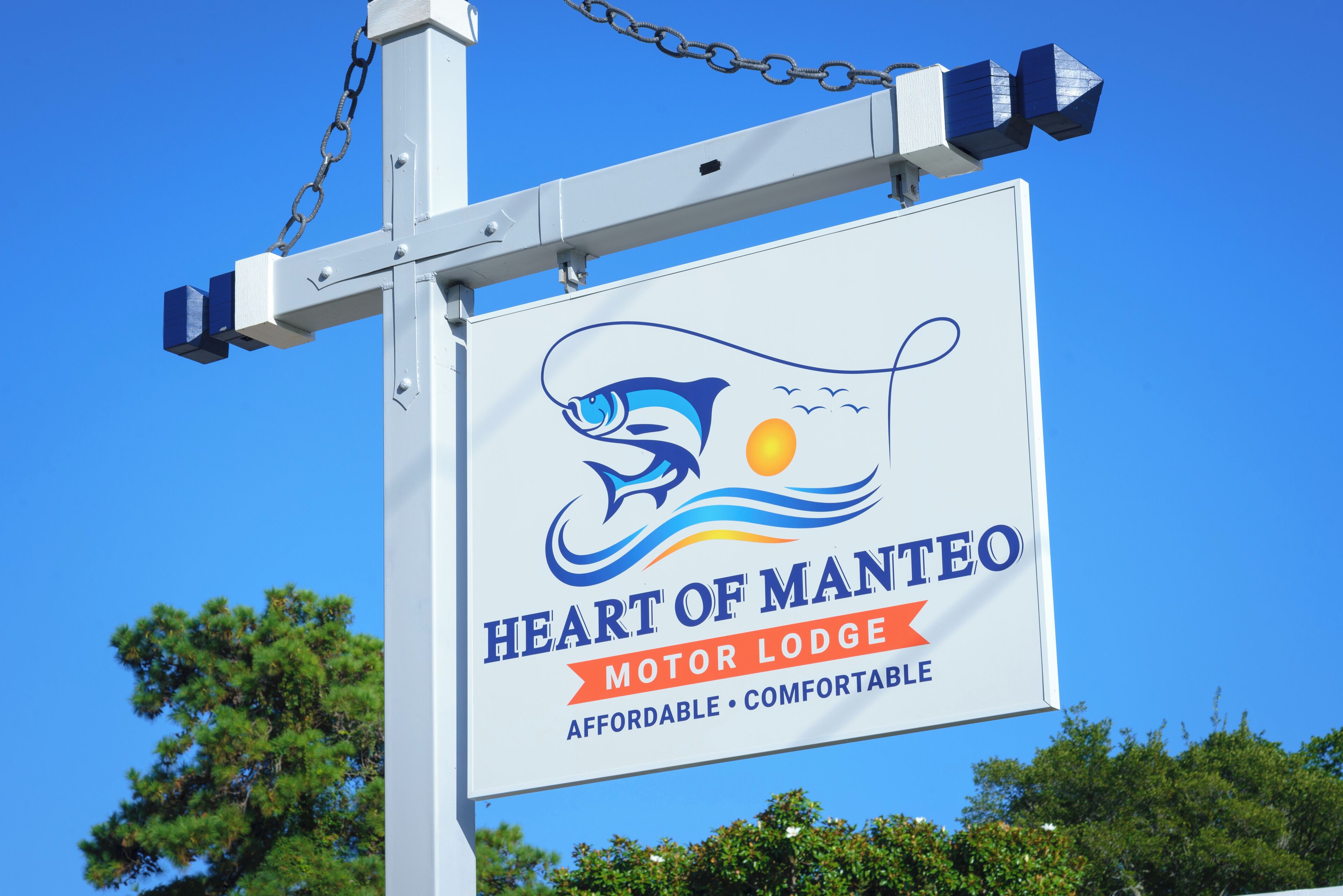 A sign for the Heart of Mantee Motor Lodge with a logo featuring a stylized fish and sun.