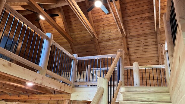 A wooden interior with a high ceiling, a fan, and a staircase with metal railings.