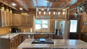 A modern kitchen with wooden cabinets, a marble island, stainless steel appliances, and a bar area with stools.