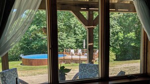 A room with large windows overlooking a backyard with a wooden deck, a hot tub, and outdoor furniture.