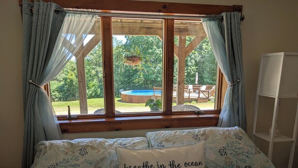 A bedroom with a bed, a window with curtains, and a view of a pool and garden.