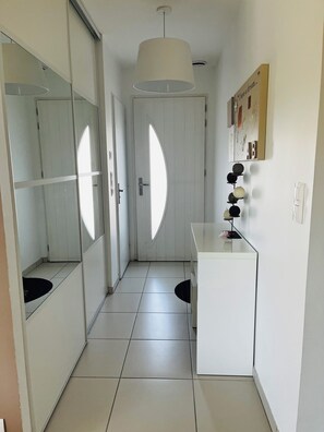 A hallway with a white door, a mirror, a pendant light, and a small table with a few items on it. - Villa with a garden in a charming village near Avignon (Entraigues-sur-la-Sorgue)