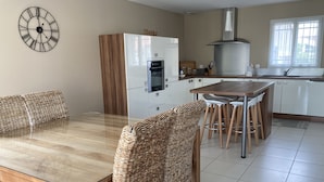 A modern kitchen with a dining area, featuring a wooden table, wicker chairs, a built-in oven, and a clock on the wall. - Villa with garden in charming village near Avignon (Entraigues-sur-la-Sorgue)