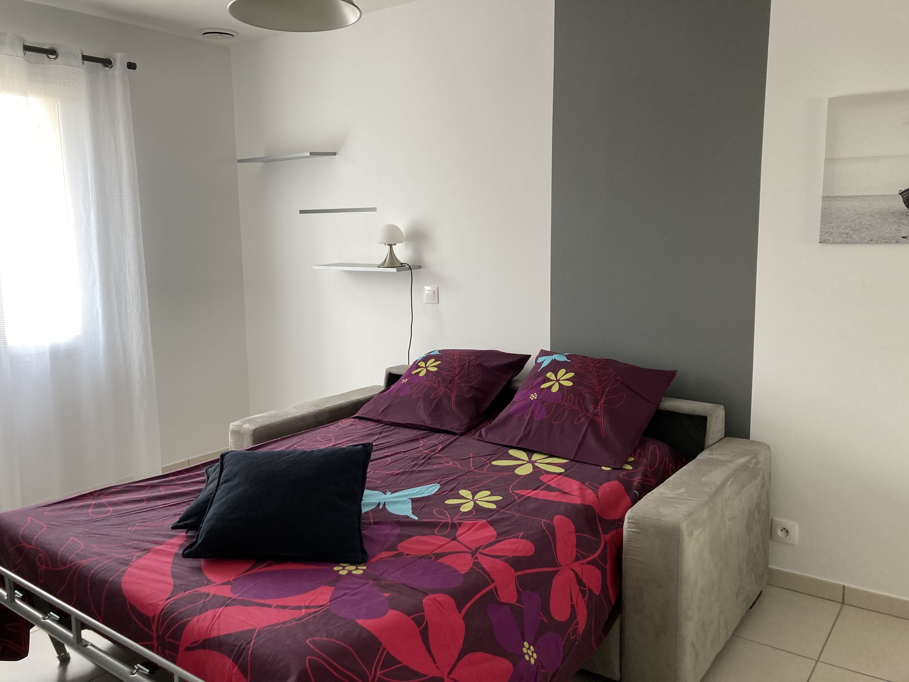 Une chambre à coucher comprenant un lit, une table de chevet, une lampe et une étagère fixée au mur.