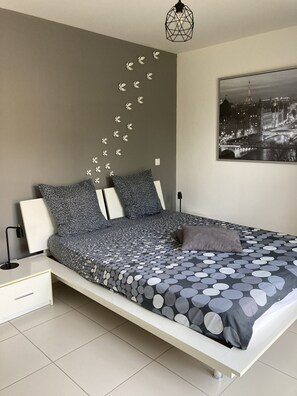 Ein modernes Schlafzimmer mit Bett, Nachttischen, einer Lampe, einer Wandleuchte und einem Stadtbild.