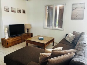 A living room with a sofa, a coffee table, a TV on a wooden cabinet, and a window with curtains. - Villa with a garden in a charming village near Avignon (Entraigues-sur-la-Sorgue)