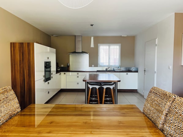 A modern kitchen with white cabinets, a wooden dining table, and a large window. - Villa with a garden in a charming village near Avignon (Entraigues-sur-la-Sorgue)