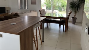 A modern kitchen with a wooden countertop, bar stools, and a dining area with a bench and chairs. - Villa with garden in charming village near Avignon (Entraigues-sur-la-Sorgue)