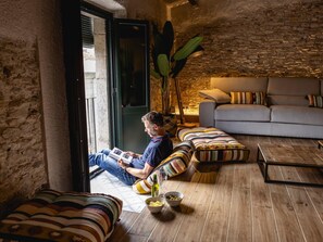 Una sala de estar acogedora con una pared de piedra, un sofá, una mesa de centro con aperitivos y una persona leyendo un libro.