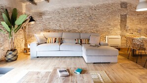 Un salon chaleureux avec un mur en pierre, un canapé blanc, une table basse et une plante.