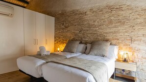 Une chambre à coucher avec un grand lit, un plancher en bois, un mur en pierre et une table de chevet avec une lampe.
