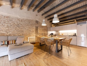 Un espacio de sala cómodo con pared de piedra, un sofá, una mesa de comedor con sillas y una cocina con gabinetes y electrodomésticos blancos.