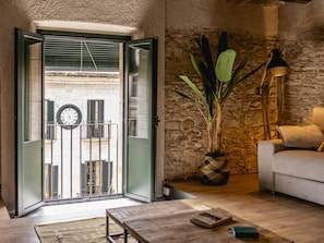 Puerta abierta que da a un balcón con un reloj, una planta en maceta, un sofá y una mesa de centro.