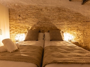 Una habitación acogedora con techo de pared de piedra, dos camas con ropa de cama estampada y lámparas de noche.