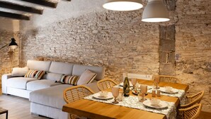 Un coin repas rustique avec une table en bois dressée pour quatre personnes, un canapé et un mur en pierre en arrière-plan.