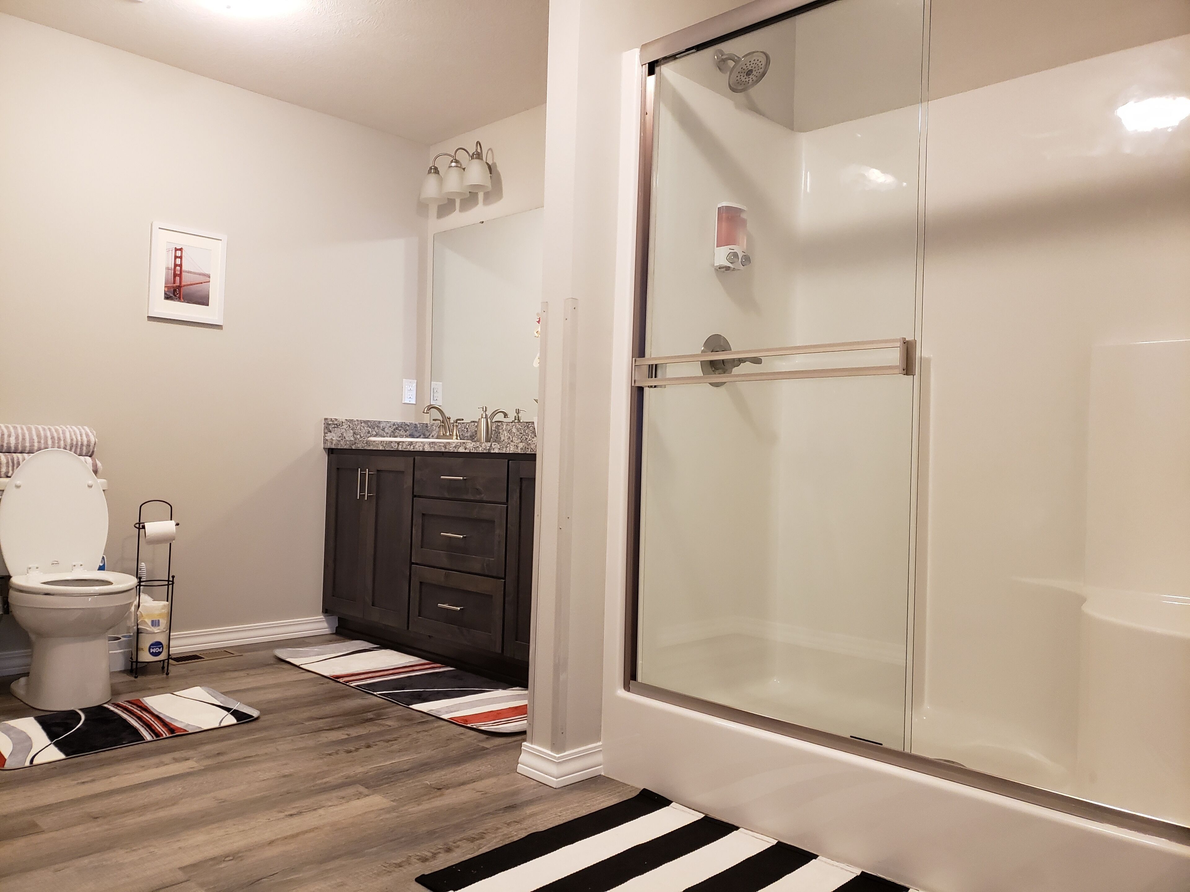 Een badkamer met toilet, wastafel, donkere kastjes, een glazen douchecabine en een gestreept vloerkleed.