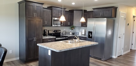 A modern kitchen with dark cabinets, stainless steel appliances, granite countertops, and pendant lighting.
