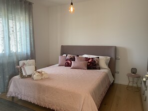 Cama bem arrumada com colcha rosa, travesseiros e um cesto decorativo.