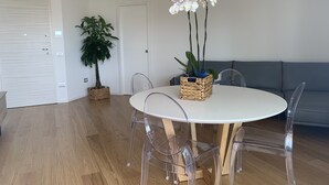 Een moderne eetruimte met een ronde tafel, transparante stoelen, een gevlochten plantenmand en een potplant.