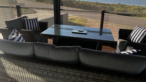 A patio with wicker furniture, a glass table, and a view of the sea. - Beautiful private beachfront home overlooking the stunning Boston Bay and PL (North Shields)