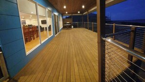 A wooden deck with a railing, a dining area with chairs and a table, and a view of the sea. - Beautiful private beachfront home overlooking the stunning Boston Bay and PL (North Shields)