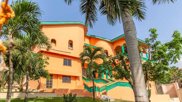 A multi-story building with a curved facade, green accents, and palm trees in the foreground.