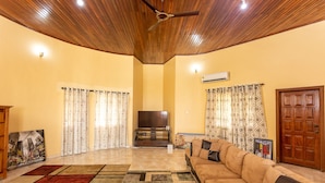 A living room with a wooden ceiling, a large sofa, a flat-screen TV, and a painting on the wall.