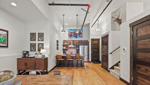 Una cocina moderna con una isla central, iluminación colgante y una escalera que lleva a un altillo.