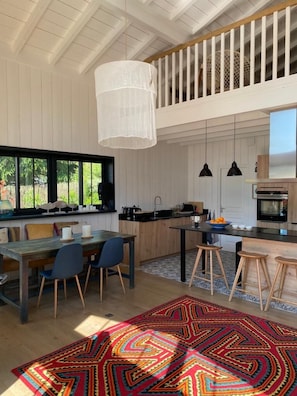 A spacious kitchen with a dining area, a large window, and a colorful rug.