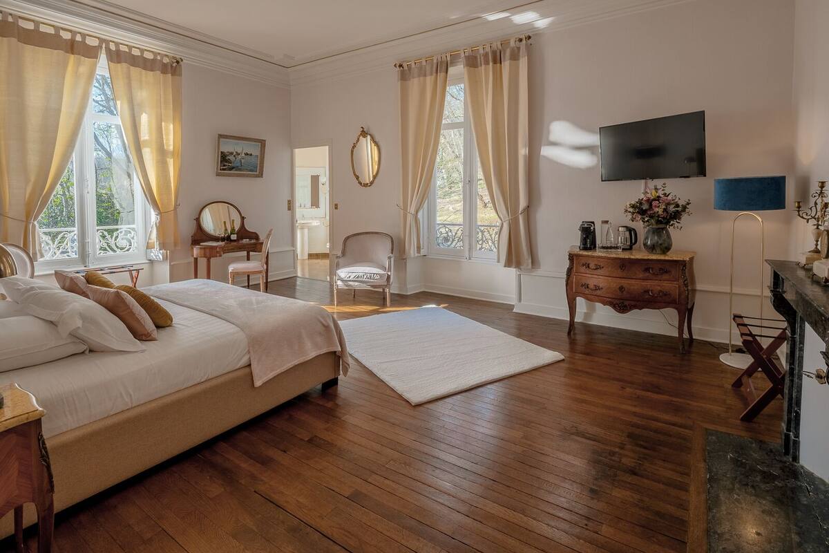Ein geräumiges Schlafzimmer mit einem großen Bett, einem Schminktisch, einem Sessel, einem Fernseher und einem Kamin.