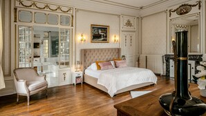 Un dormitorio lujoso con una cama grande, un sillón, una chimenea y un espejo.