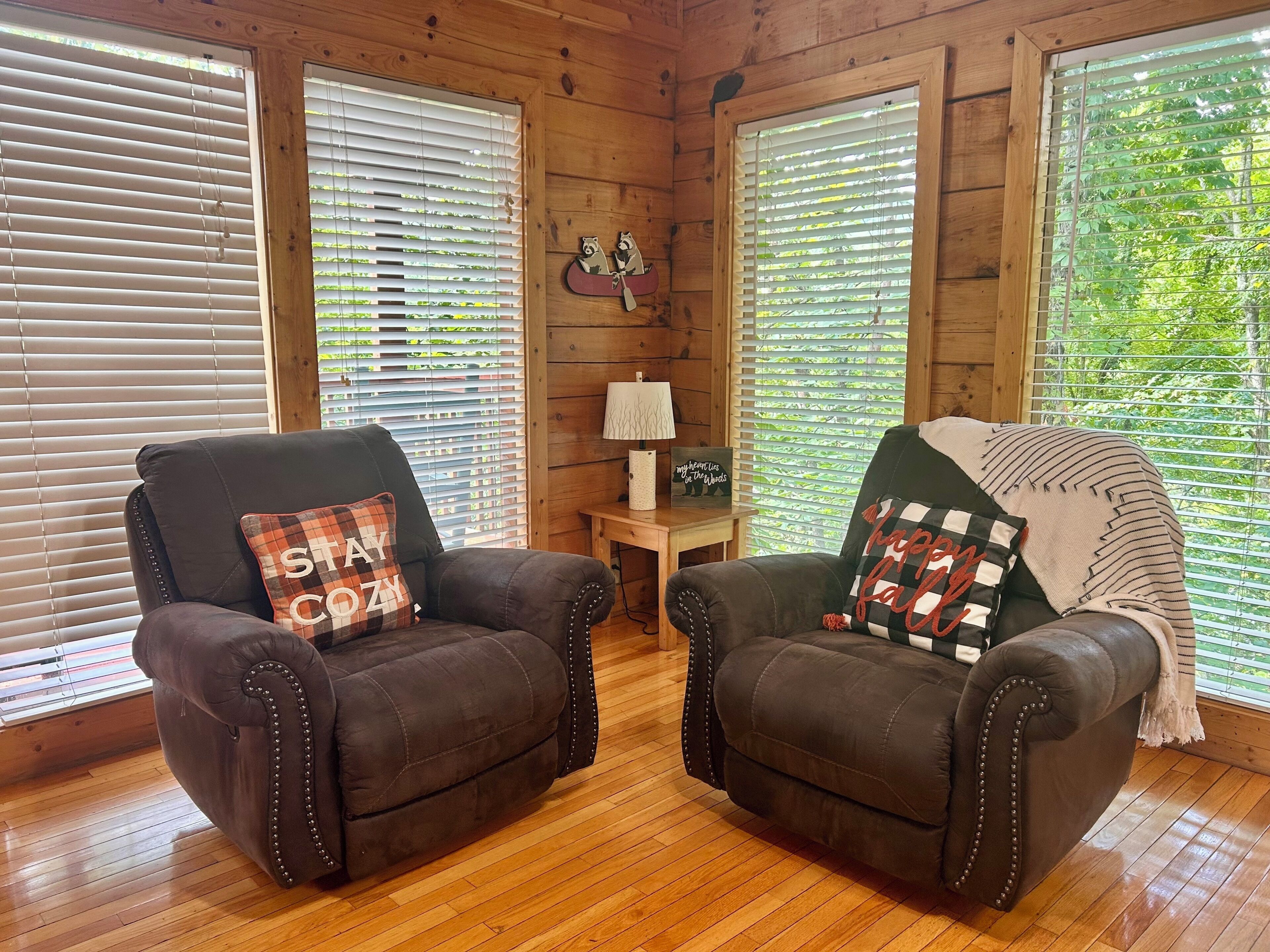 A cozy room with two leather armchairs, wooden flooring, and large windows with blinds.