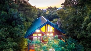 Une cabane entourée d’une forêt dense, dotée d’un balcon visible et de grandes fenêtres.