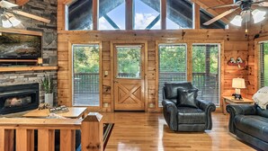 Un intérieur de chalet chaleureux avec une cheminée en pierre, des meubles en cuir et de grandes fenêtres.