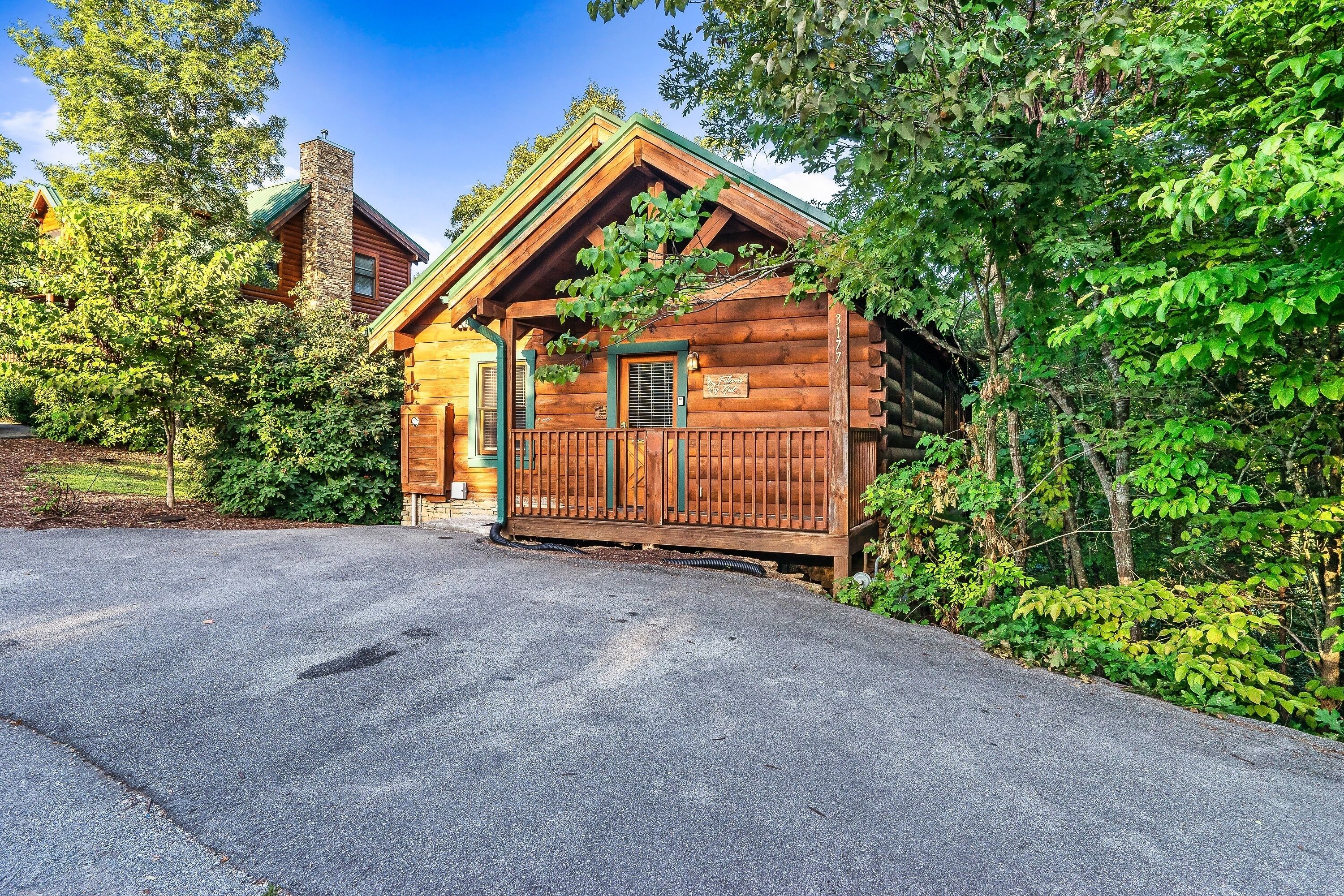 A log cabin with a front porch and a chimney, surrounded by trees.