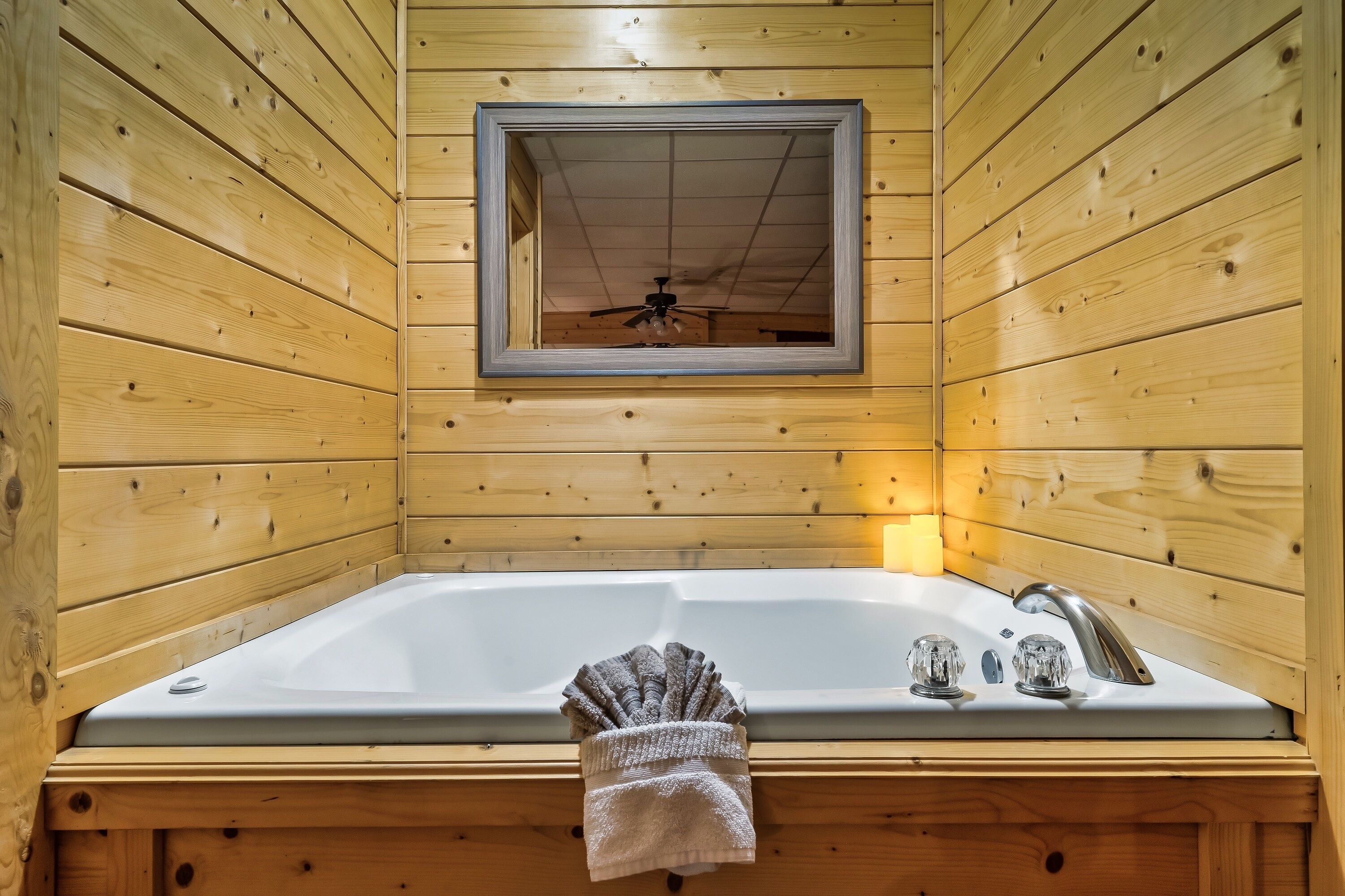 Una cabaña de madera con una bañera grande, un espejo y un ventilador de techo.