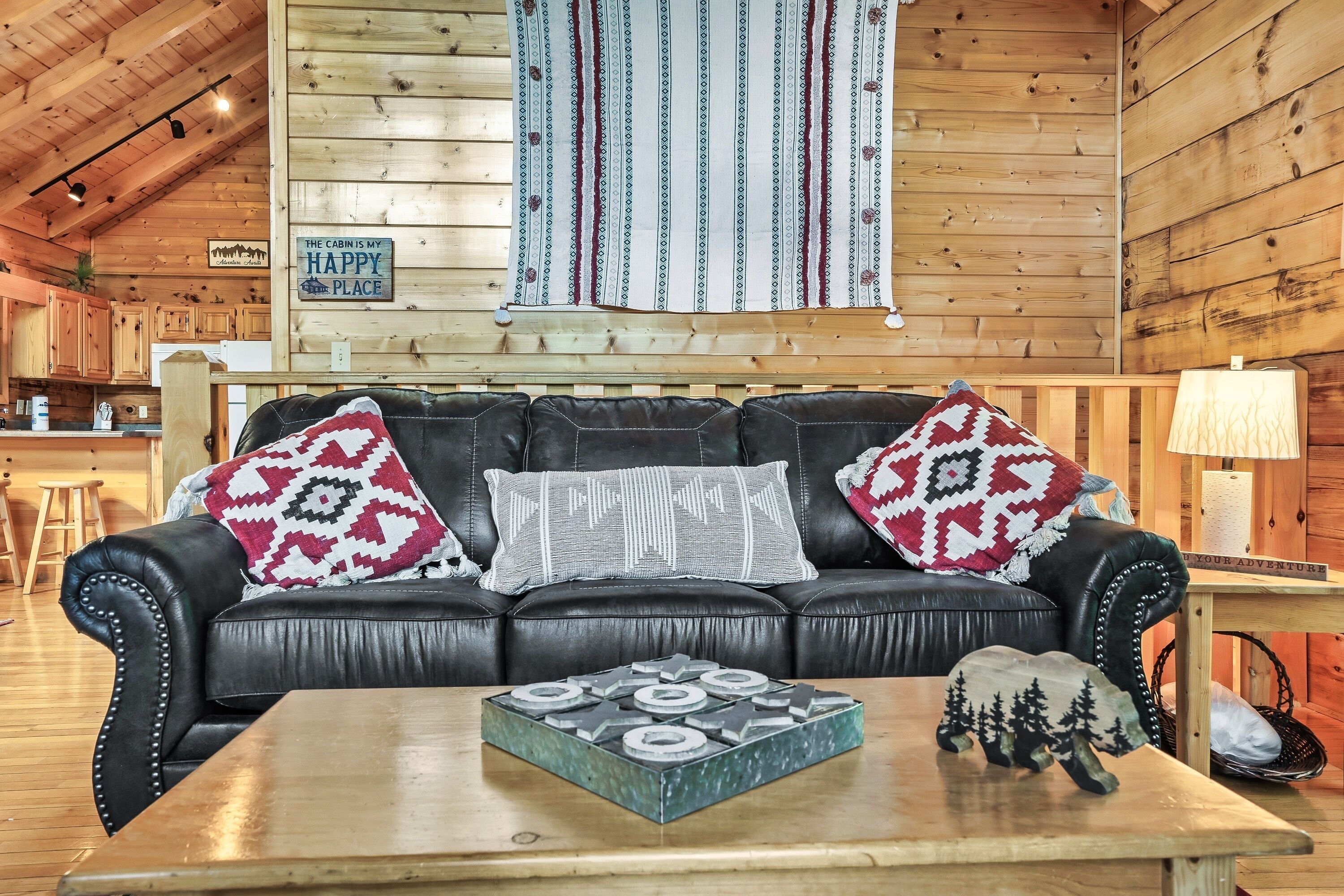 L’intérieur chaleureux d’un chalet avec un canapé en cuir noir, des coussins décoratifs à motifs et un plafond en bois rustique.