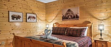 A wooden-paneled room with a bed, two framed animal pictures, a wall-mounted lamp, and a ceiling fan.