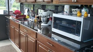 Cucina con mobili in legno, forno a microonde, fornello e diversi utensili.