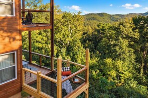 A multi-level wooden cabin with a balcony overlooking a forested mountain area.