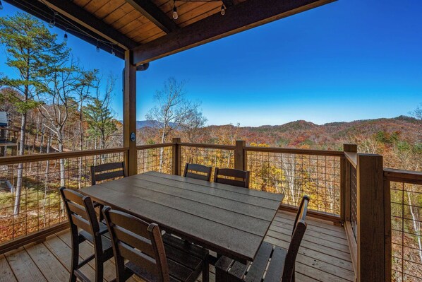 A wooden deck with a table and chairs, overlooking a mountainous landscape.