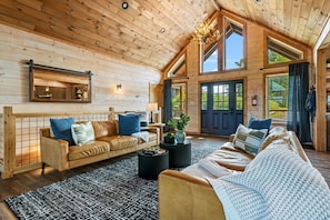 A cozy log cabin interior with a large living area, wooden walls, and a high ceiling.
