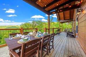 Una terraza de madera con una mesa dispuesta para comer, con vistas a un paisaje verde y exuberante.
