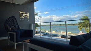 A modern hotel room with a large balcony overlooking a body of water, a hanging chair, and a sofa.