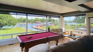 Et billardbord i et rum med store vinduer med udsigt over en sø og en badebro.