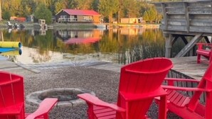 En træterrasse ved søen med røde Adirondack-stole, et bålsted og en dok, der strækker sig ud i vandet.